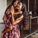 little girl wearing a long brown dress with tie sleeve with light pink lei awapuhi print hugging her mother in matching dress