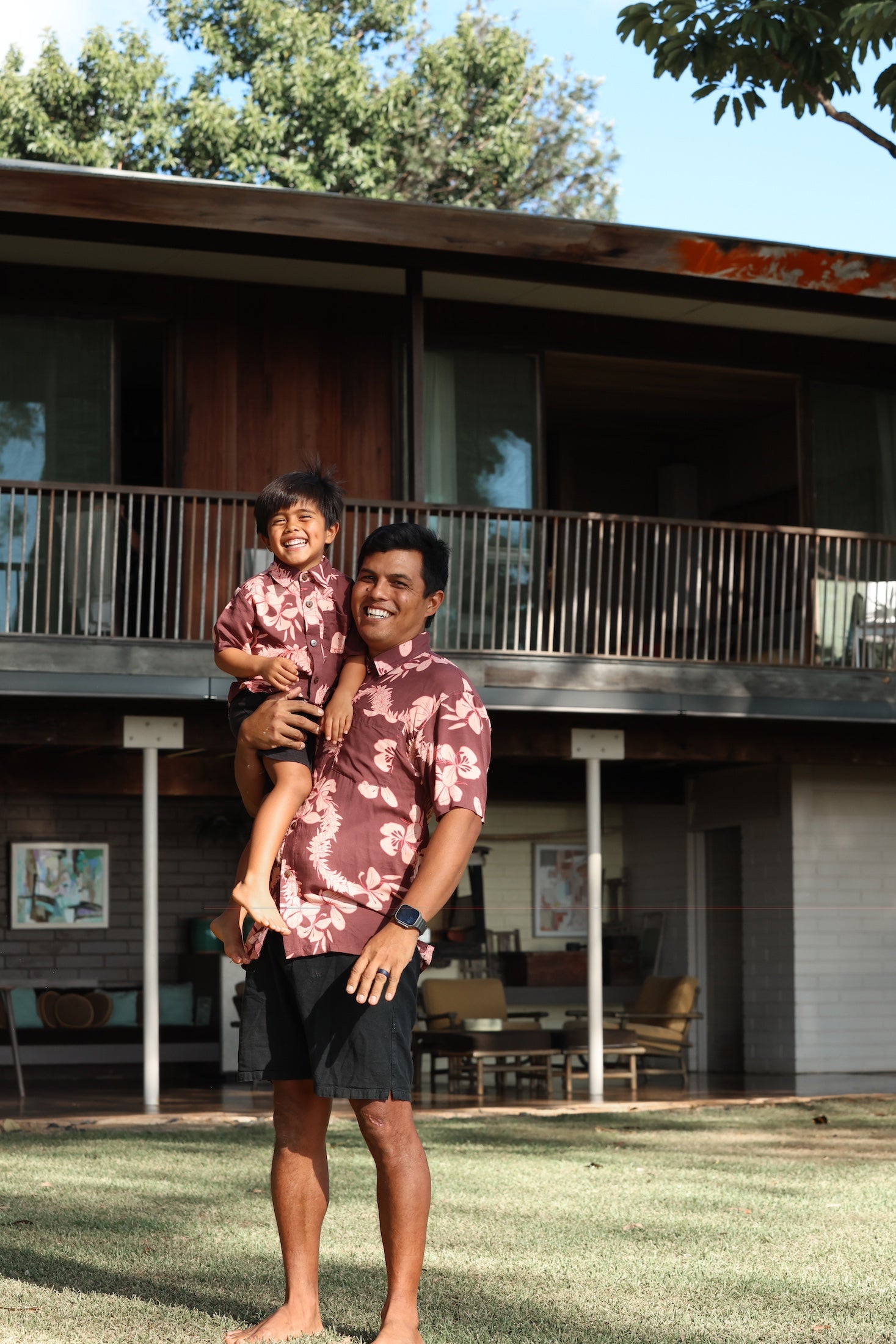 little boy wearing brown aloha shirt with pink lei awapuhi print