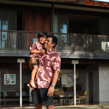 man wearing brown aloha shirt with pink lei awapuhi print