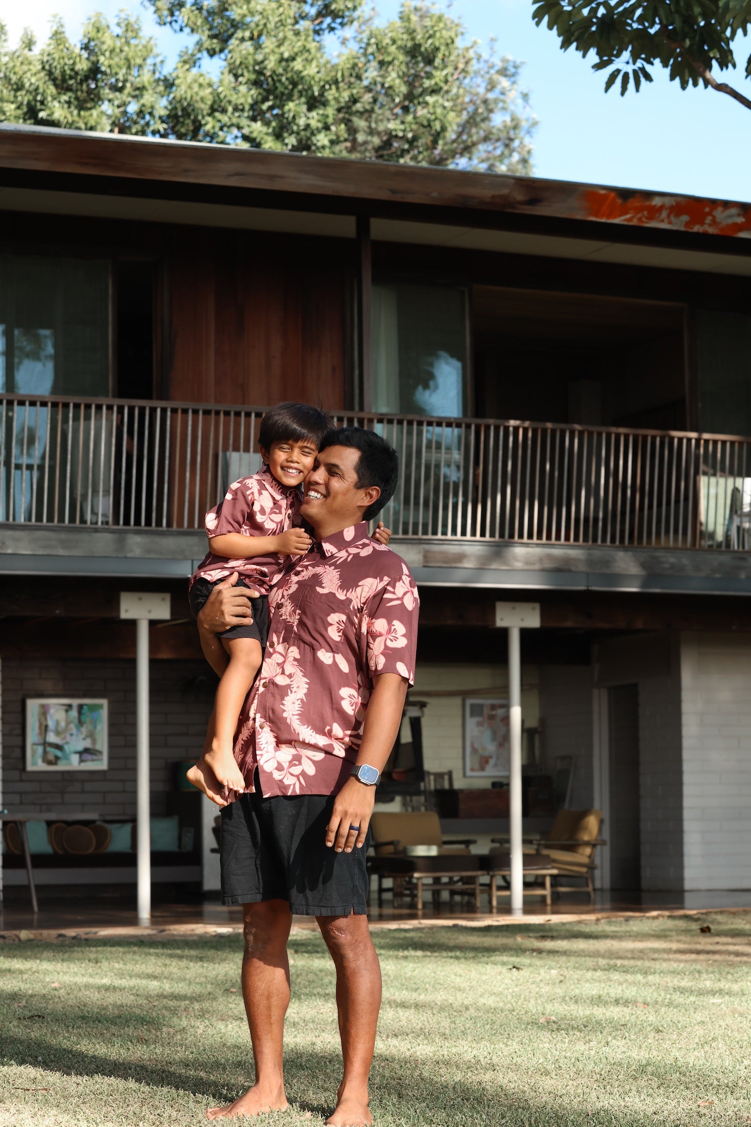 man wearing brown aloha shirt with pink lei awapuhi print