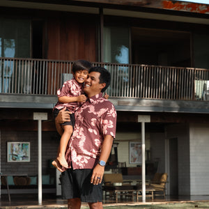 man wearing brown aloha shirt with pink lei awapuhi print