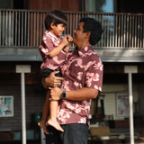 man wearing brown aloha shirt with pink lei awapuhi print