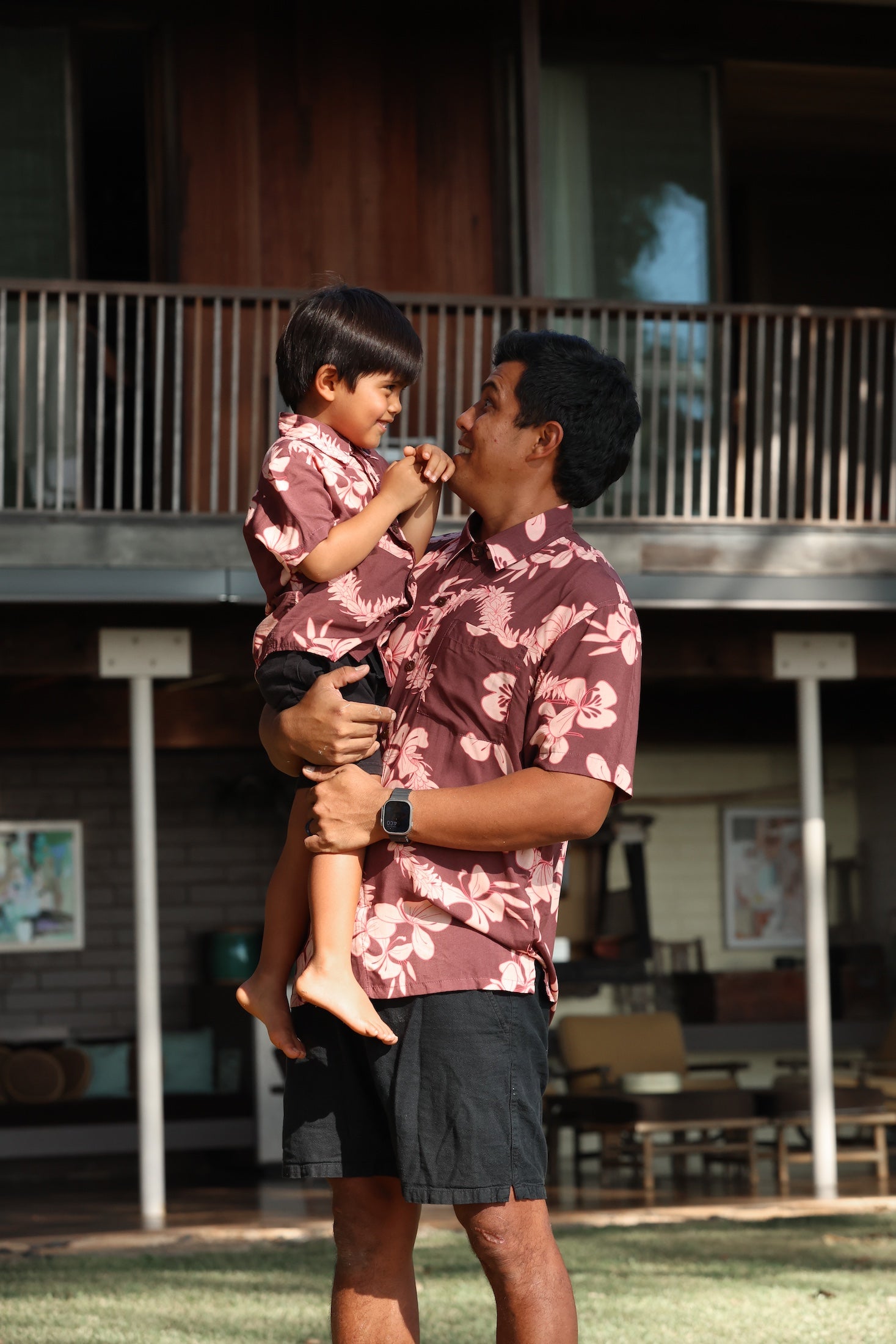 man wearing brown aloha shirt with pink lei awapuhi print