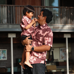 man wearing brown aloha shirt with pink lei awapuhi print