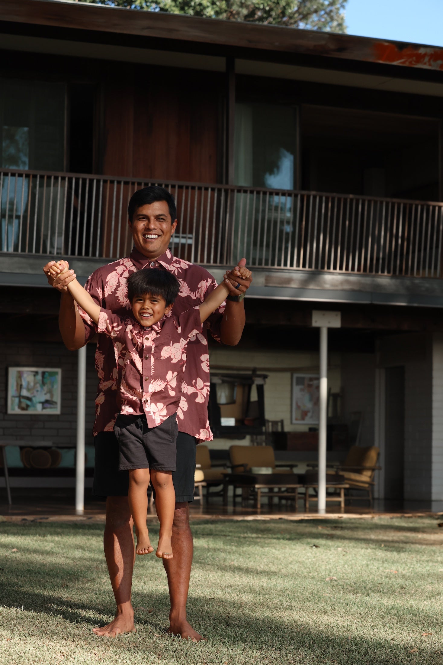 little boy wearing brown aloha shirt with pink lei awapuhi print