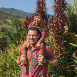 man with brown hair wearing a colorful button up aloha shirt with tropical lei print