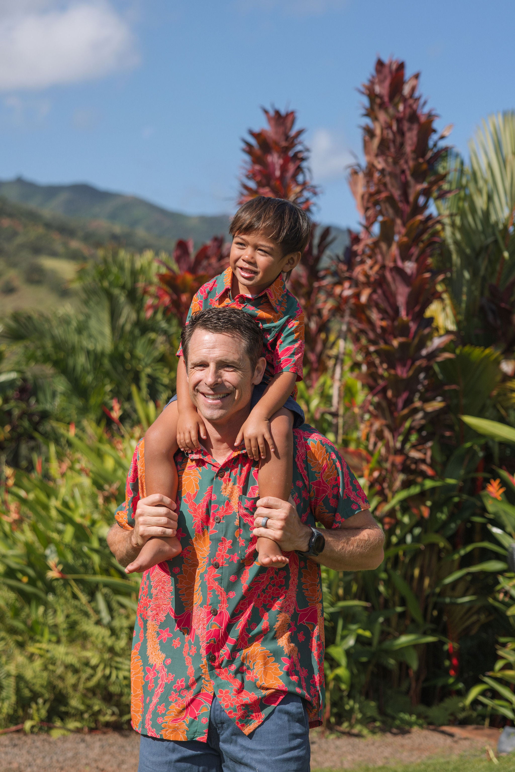 man with brown hair wearing a colorful button up aloha shirt with tropical lei print