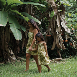 little girl wearing spaghetti strap dress in green print with naupaka pattern