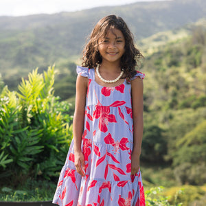 little girl with brown hair wearing a mid length dress with periwinkle background and bright red hibiscus print.