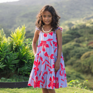 little girl with brown hair wearing a mid length dress with periwinkle background and bright red hibiscus print.