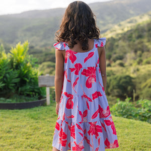 little girl with brown hair wearing a mid length dress with periwinkle background and bright red hibiscus print.