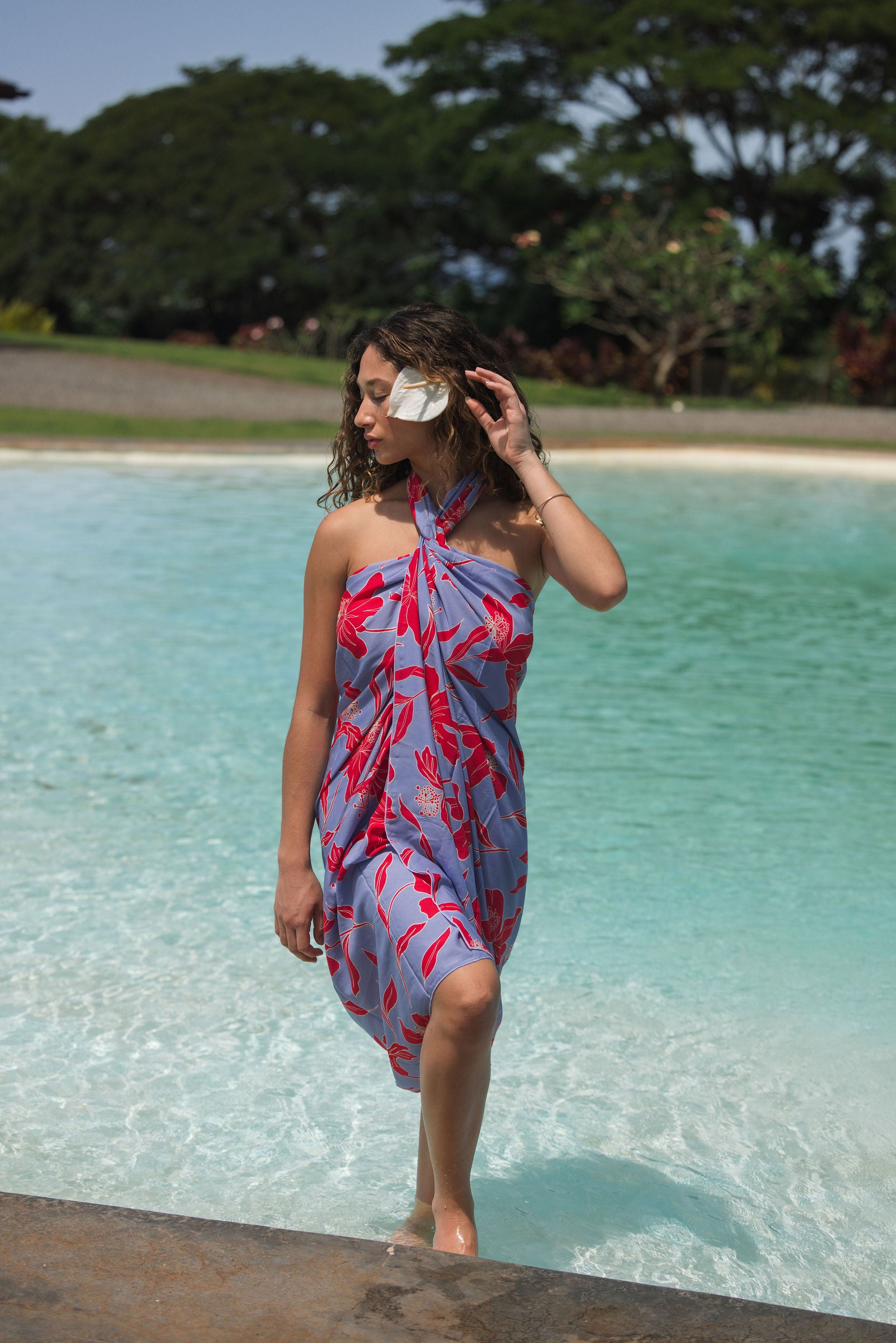 woman with brown hair wearing a pareo with periwinkle background and bright red hibiscus print.