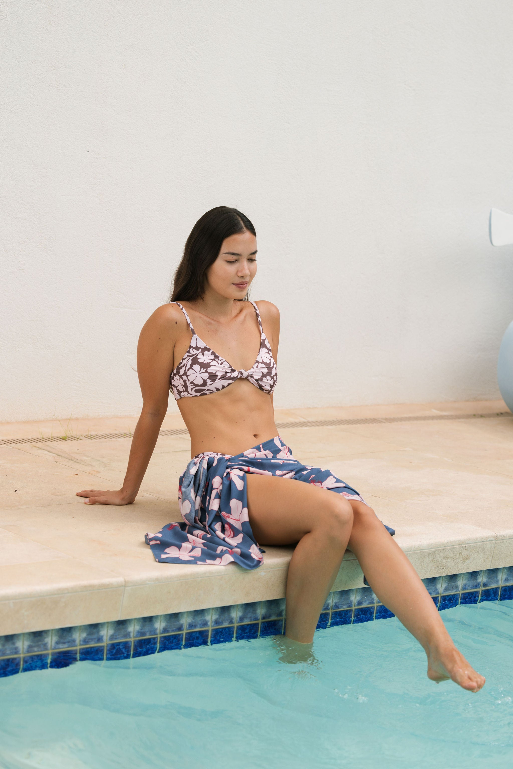 woman with black hair wearing a pareo in a navy and pink hibiscus print.