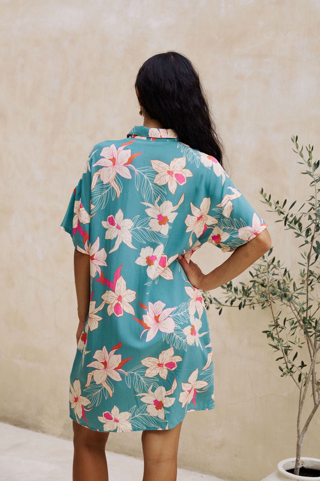 woman with brown hair wearing collared button up dress in teal with large cream colored orchids.