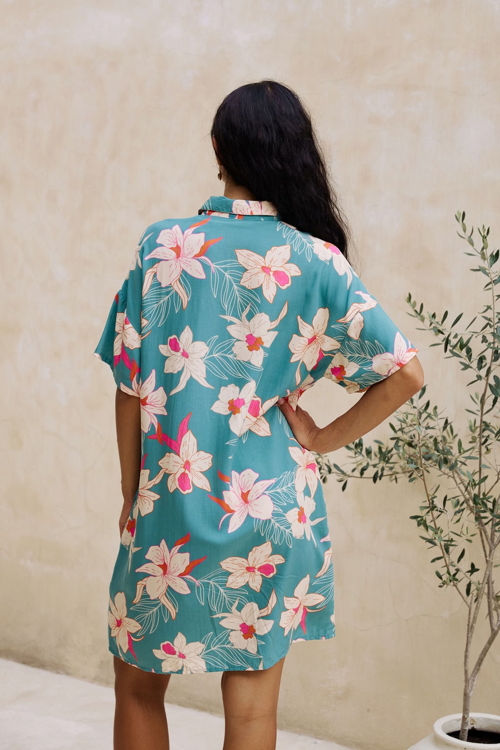 woman with brown hair wearing collared button up dress in teal with large cream colored orchids.