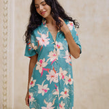 woman with brown hair wearing collared button up dress in teal with large cream colored orchids.