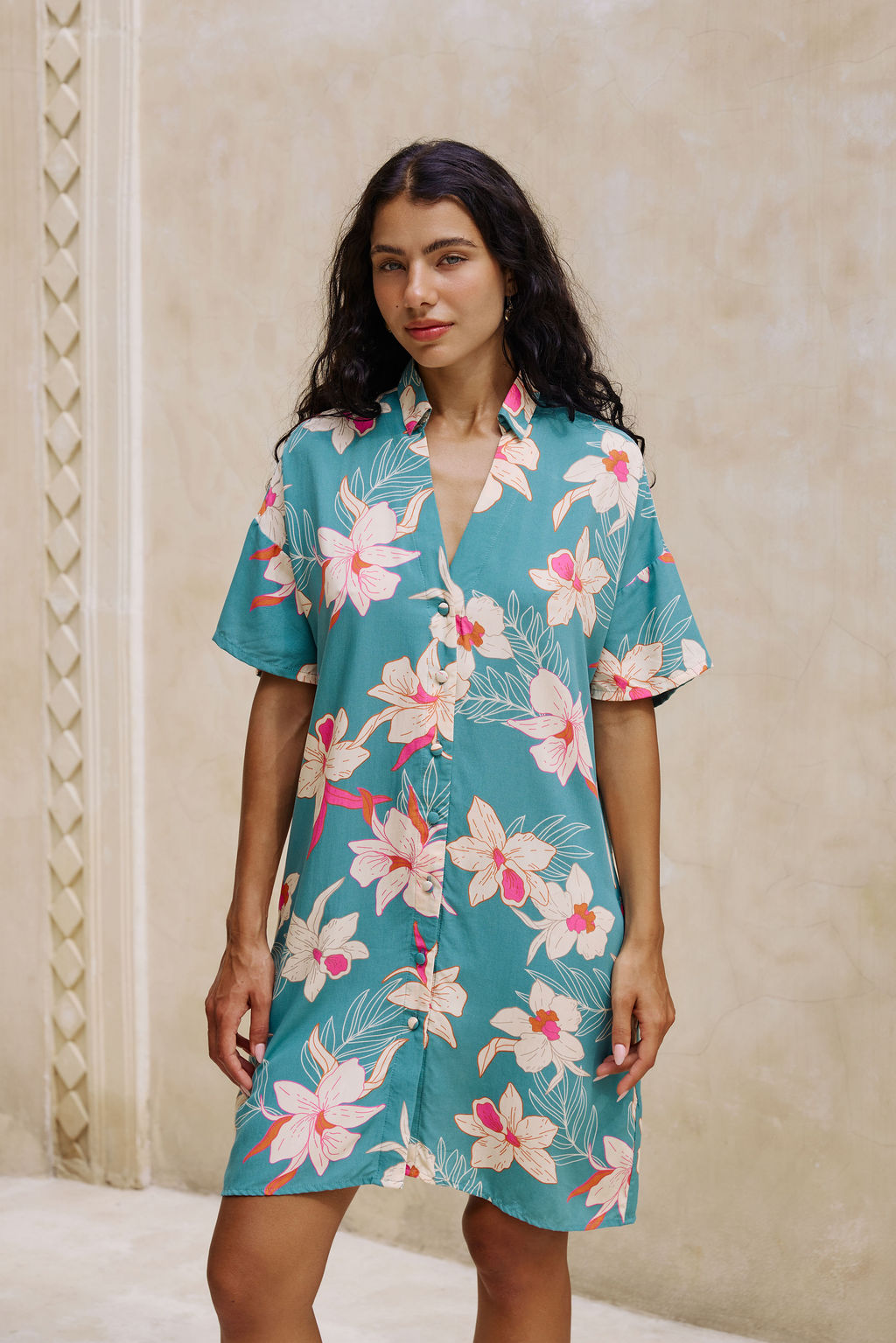 woman with brown hair wearing collared button up dress in teal with large cream colored orchids.