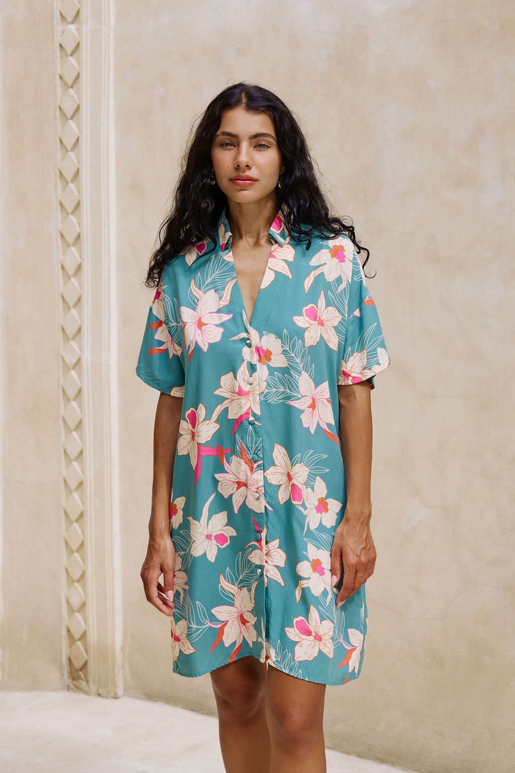 woman with brown hair wearing collared button up dress in teal with large cream colored orchids.