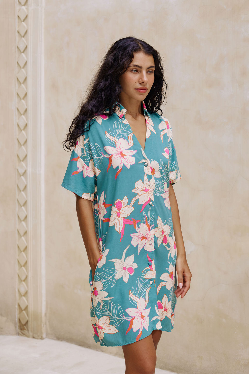 woman with brown hair wearing collared button up dress in teal with large cream colored orchids.