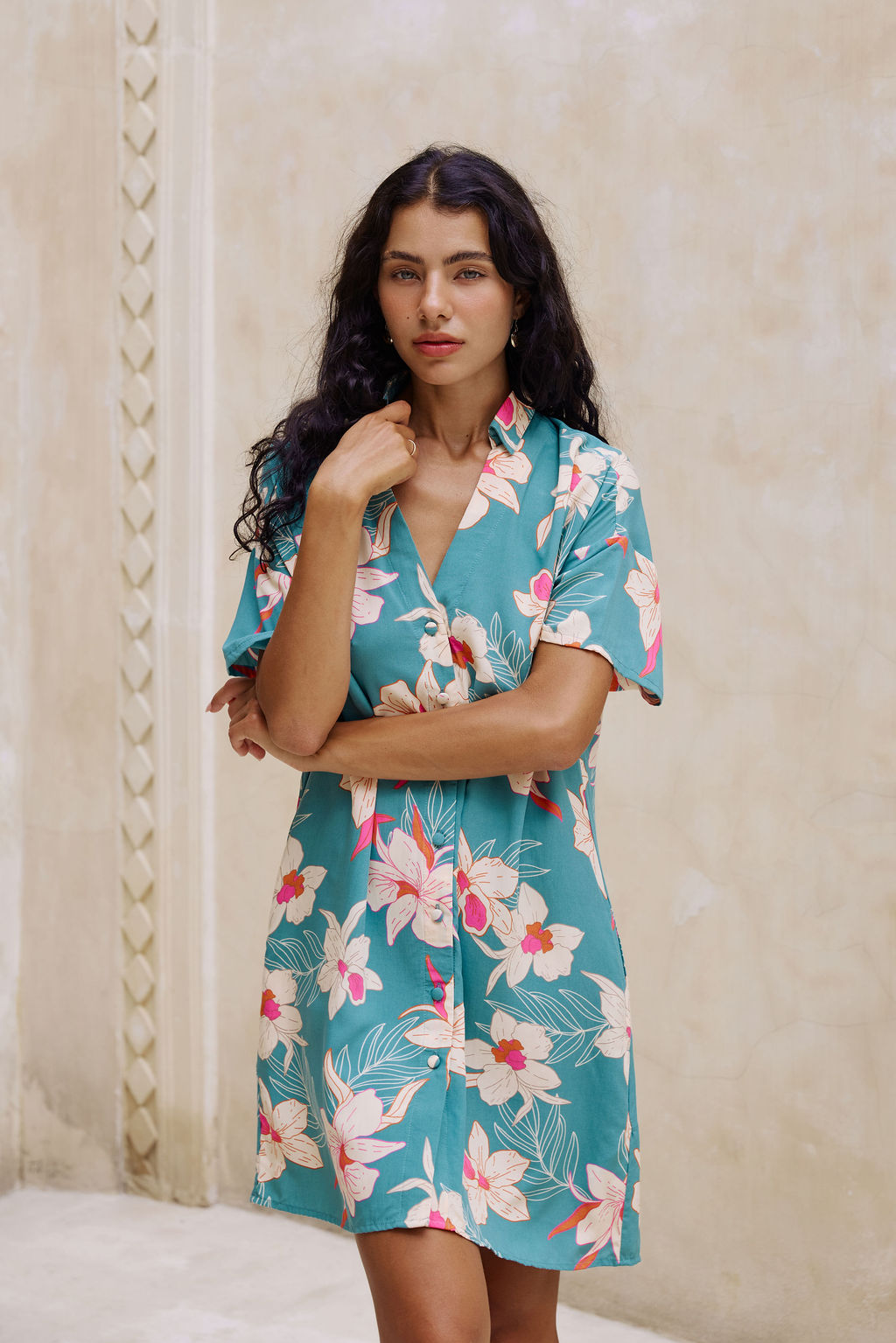 woman with brown hair wearing collared button up dress in teal with large cream colored orchids.