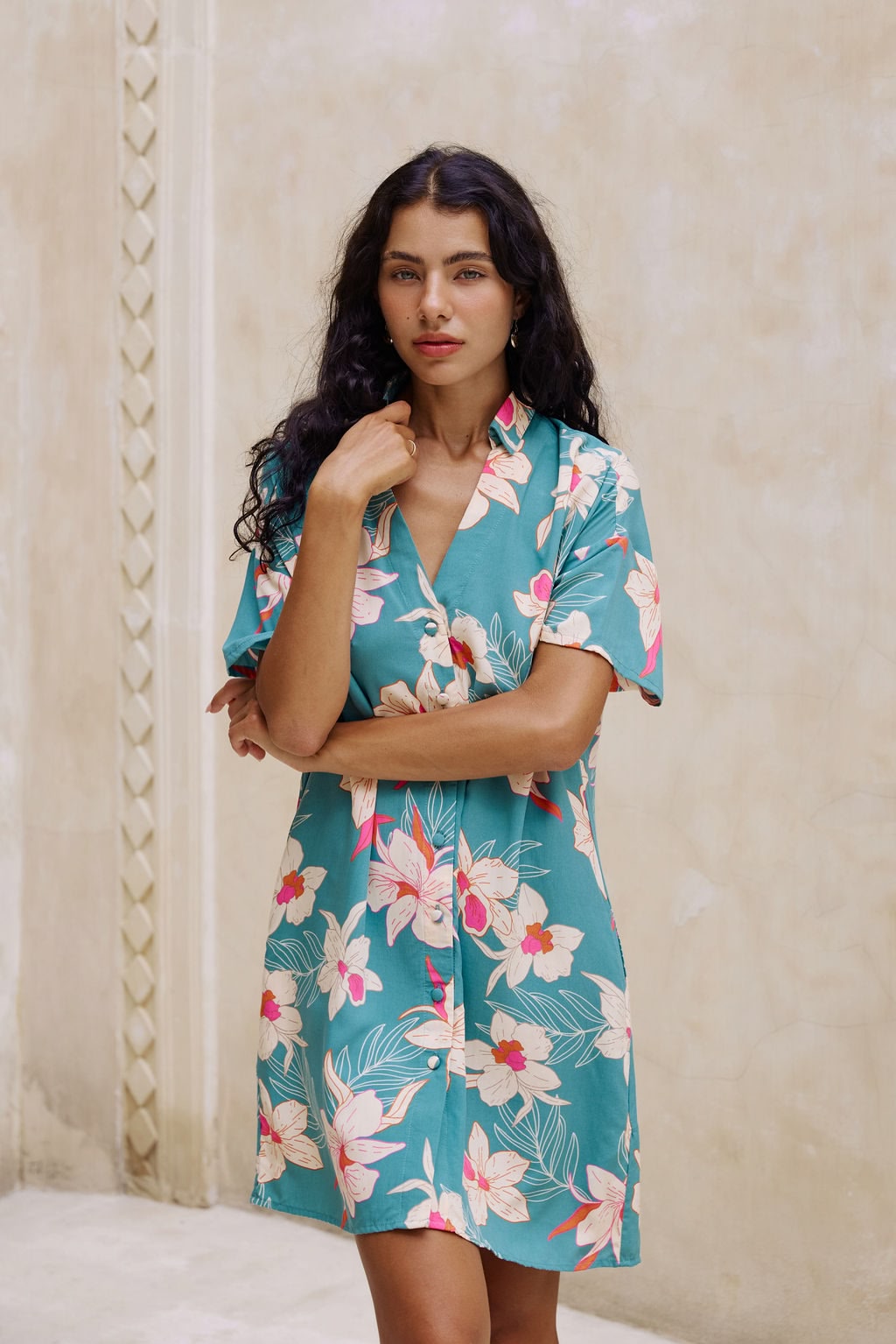 woman with brown hair wearing collared button up dress in teal with large cream colored orchids.