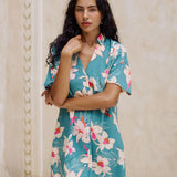 woman with brown hair wearing collared button up dress in teal with large cream colored orchids.