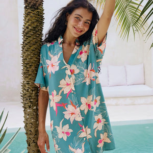 woman with brown hair wearing collared button up dress in teal with large cream colored orchids.