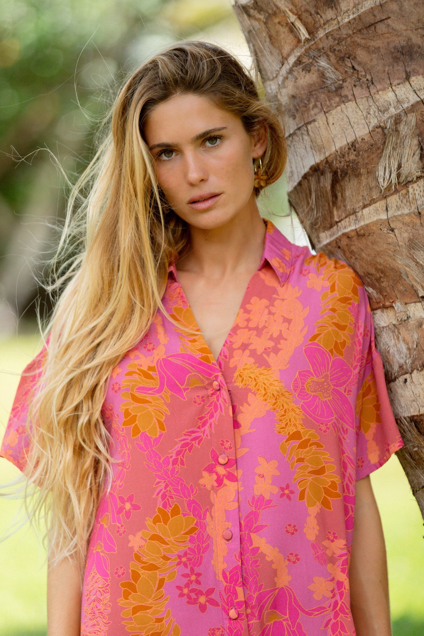 woman wearing a pink v neck button up mini dress with lei print