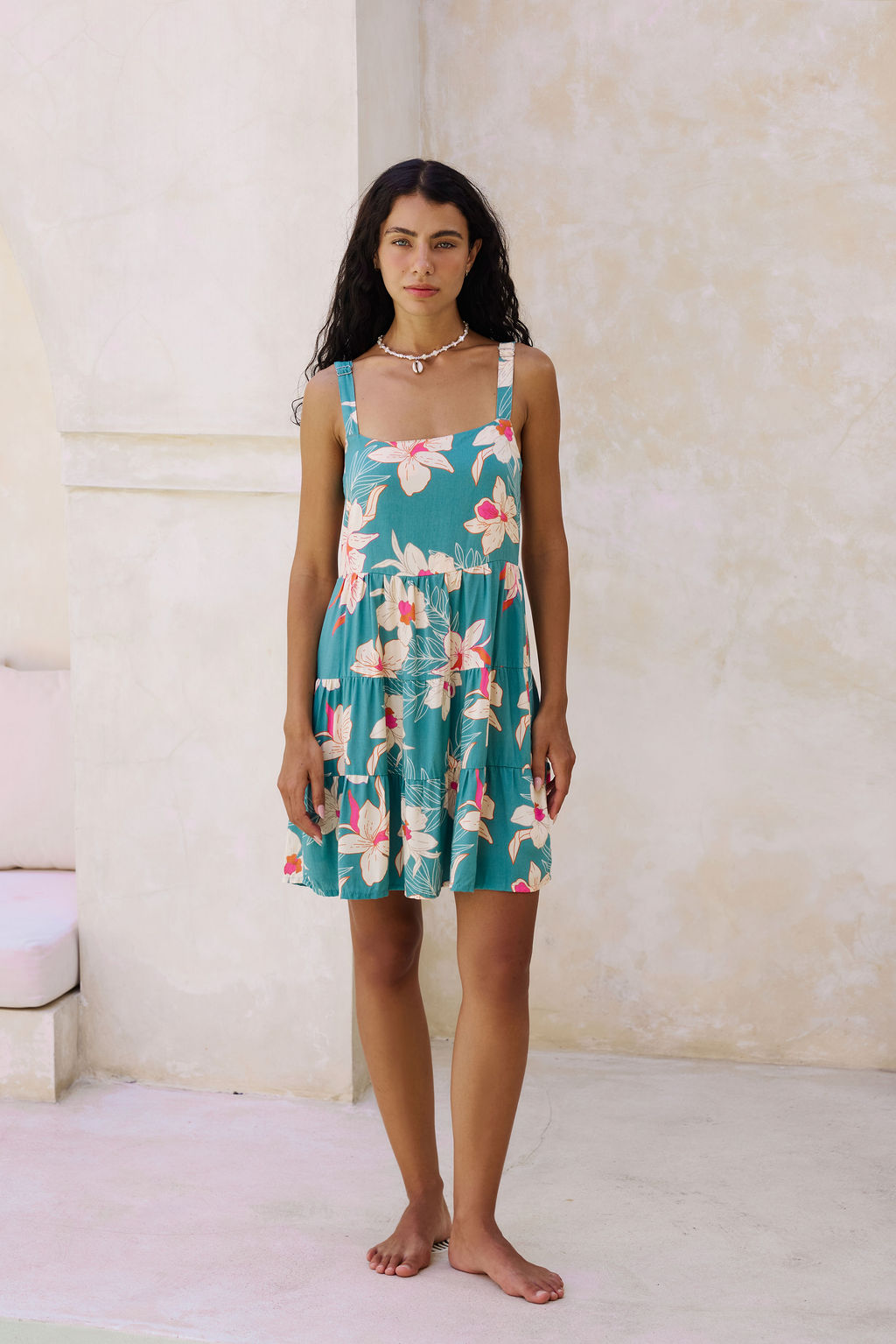 woman with brown hair wearing a tiered mini dress in teal with large cream colored orchids.