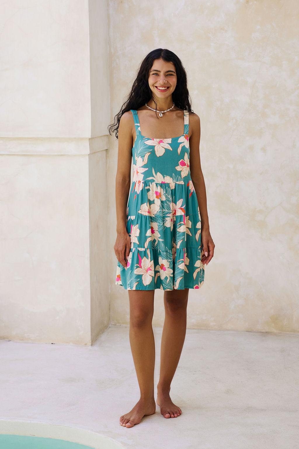 woman with brown hair wearing a tiered mini dress in teal with large cream colored orchids.