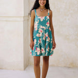 woman with brown hair wearing a tiered mini dress in teal with large cream colored orchids.