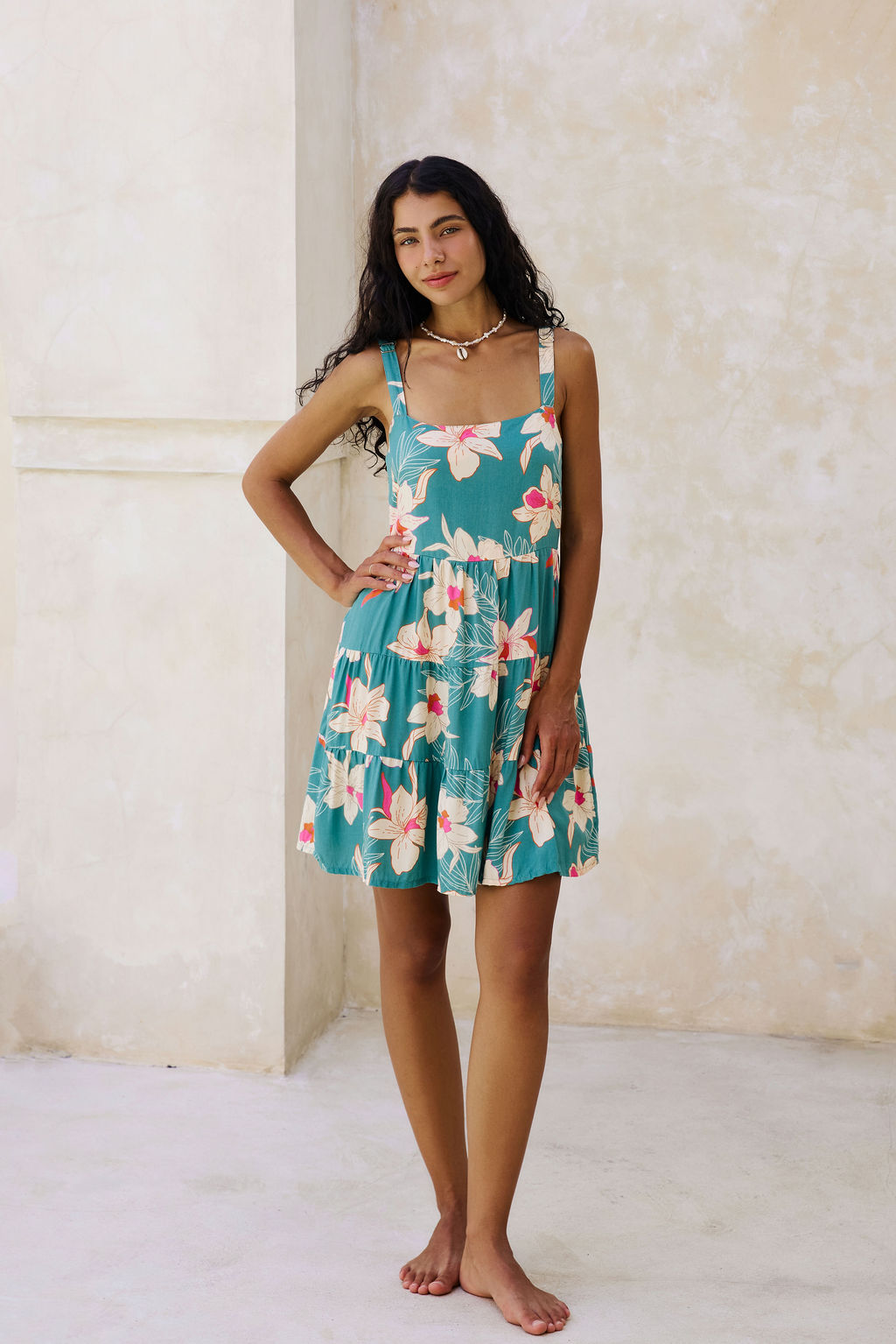 woman with brown hair wearing a tiered mini dress in teal with large cream colored orchids.