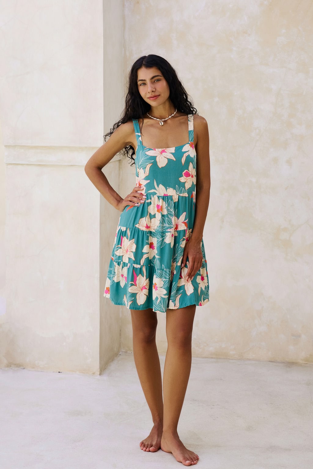 woman with brown hair wearing a tiered mini dress in teal with large cream colored orchids.