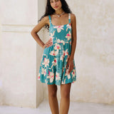 woman with brown hair wearing a tiered mini dress in teal with large cream colored orchids.