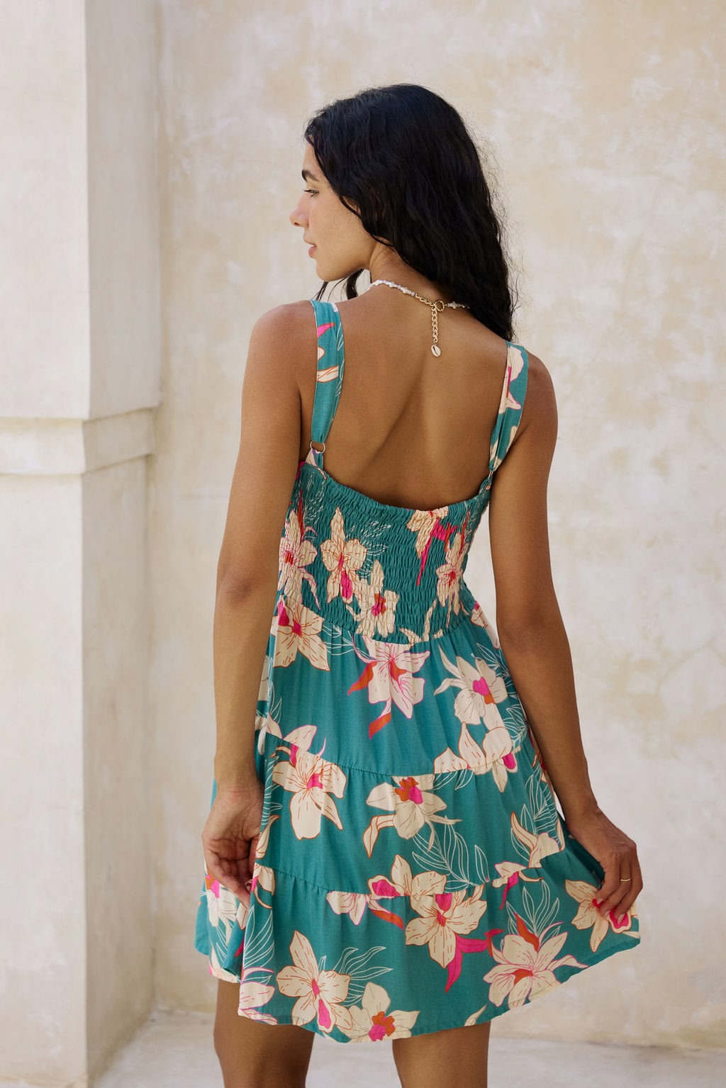 woman with brown hair wearing a tiered mini dress in teal with large cream colored orchids.