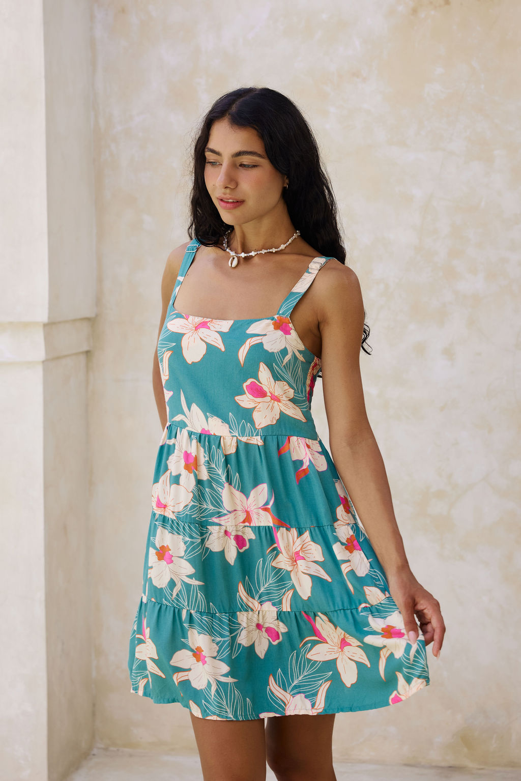 woman with brown hair wearing a tiered mini dress in teal with large cream colored orchids.