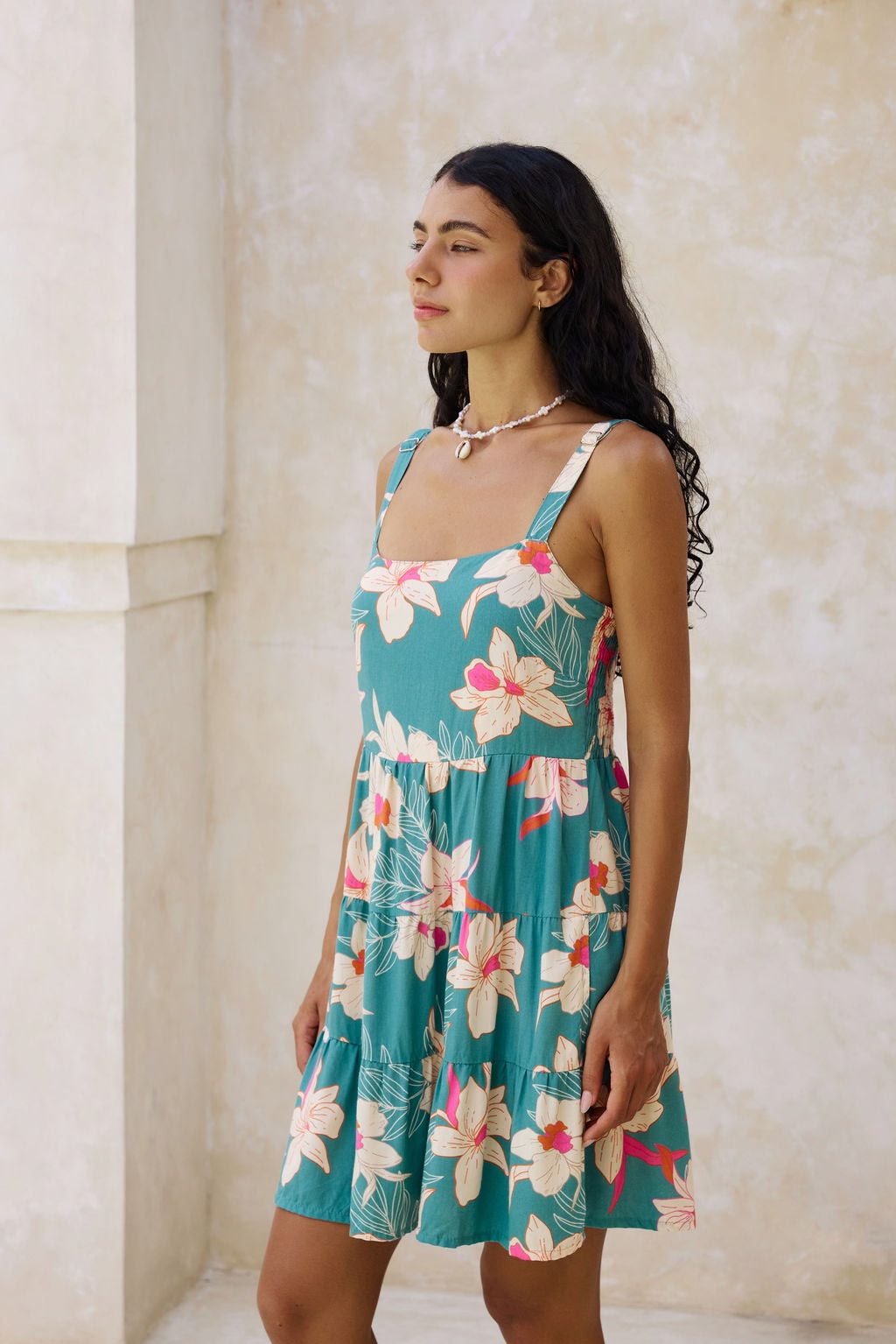woman with brown hair wearing a tiered mini dress in teal with large cream colored orchids.