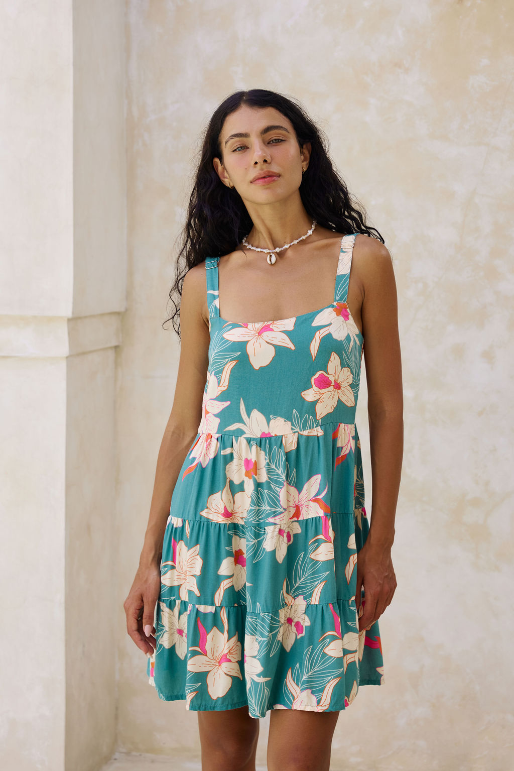 woman with brown hair wearing a tiered mini dress in teal with large cream colored orchids.