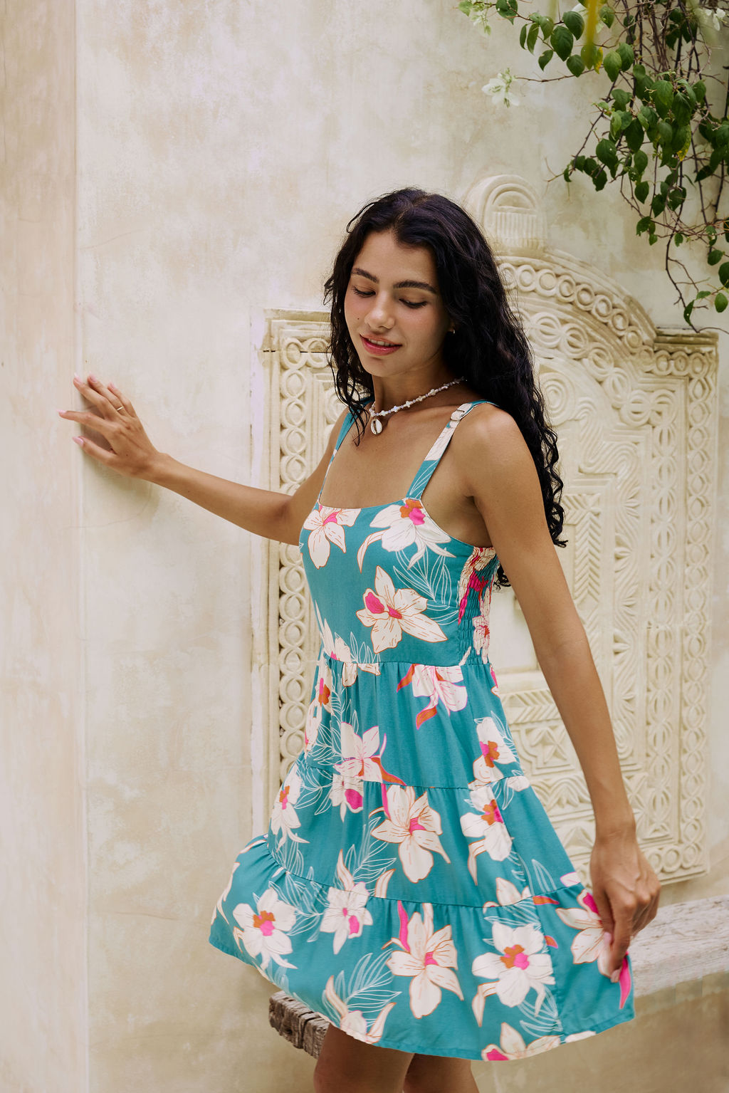 woman with brown hair wearing a tiered mini dress in teal with large cream colored orchids.