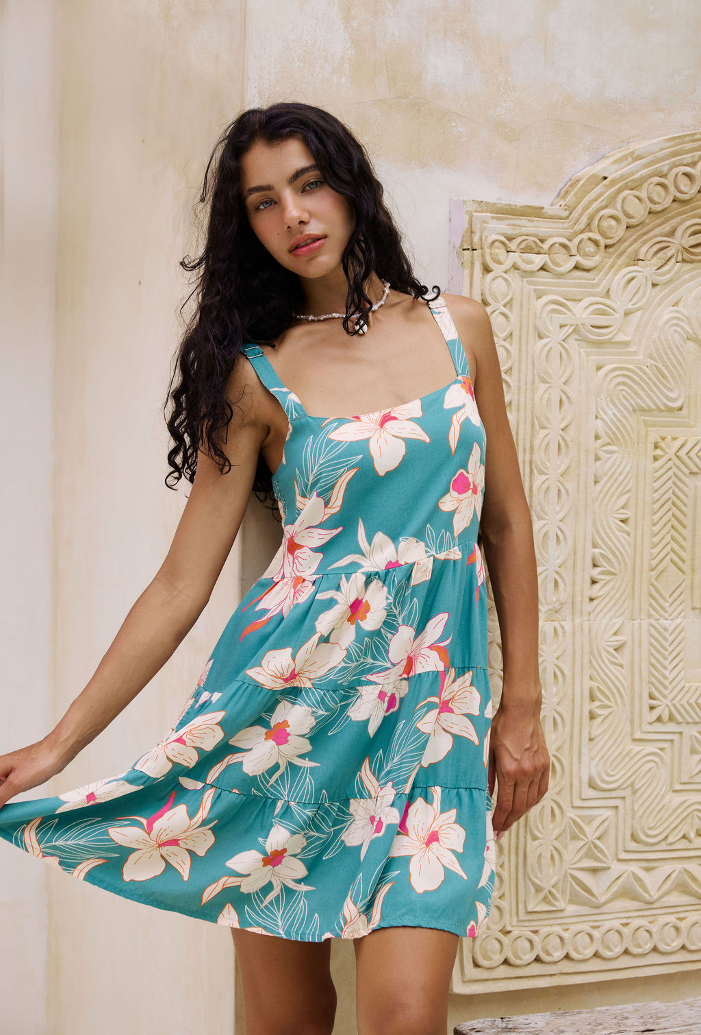 woman with brown hair wearing a tiered mini dress in teal with large cream colored orchids.