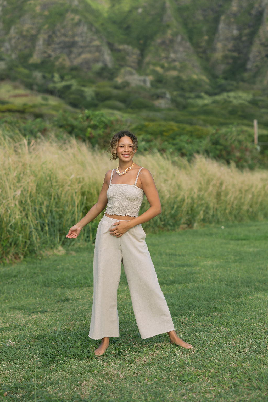 Woman wearing smocked tube top with spaghetti straps and loose pant in beige linen.