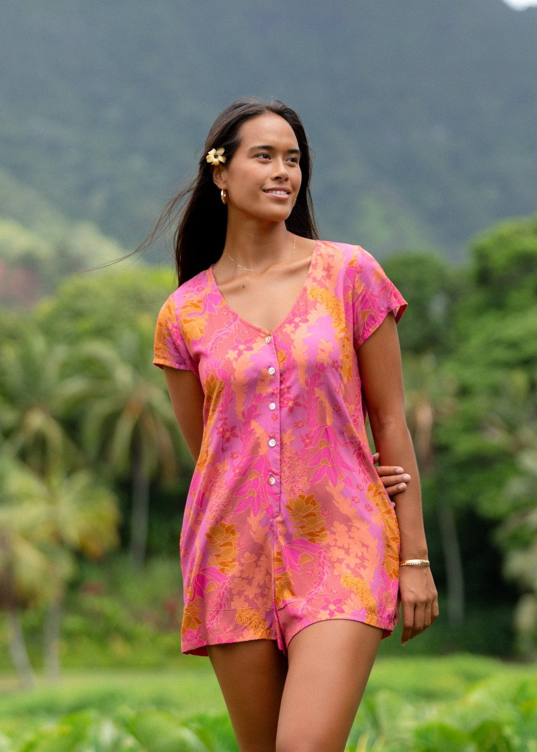 woman wearing a pink button up romper with sleeves with lei print