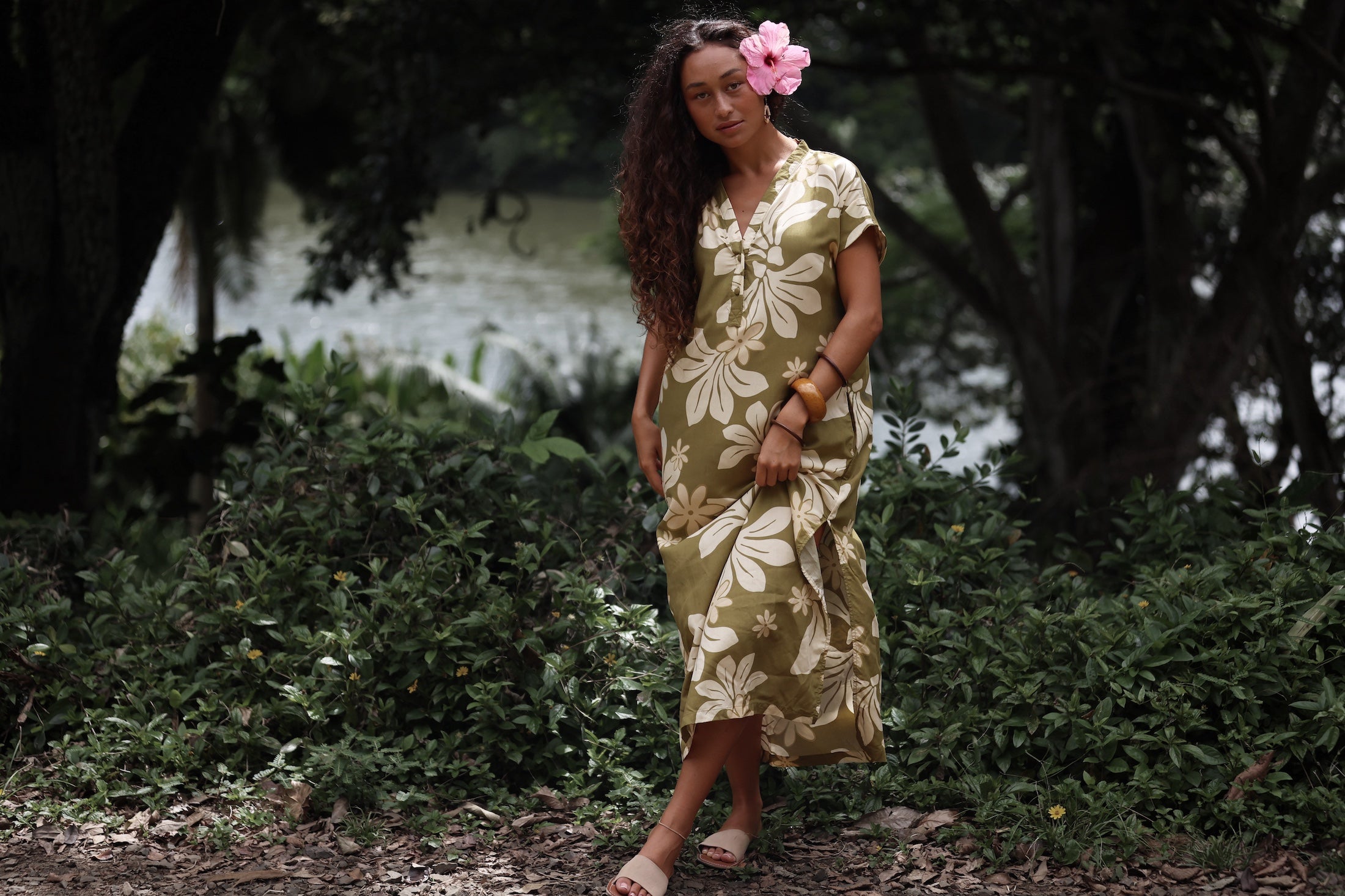 woman with brown hair wearing a maxi dress in a green color with naupaka pattern throughout.
