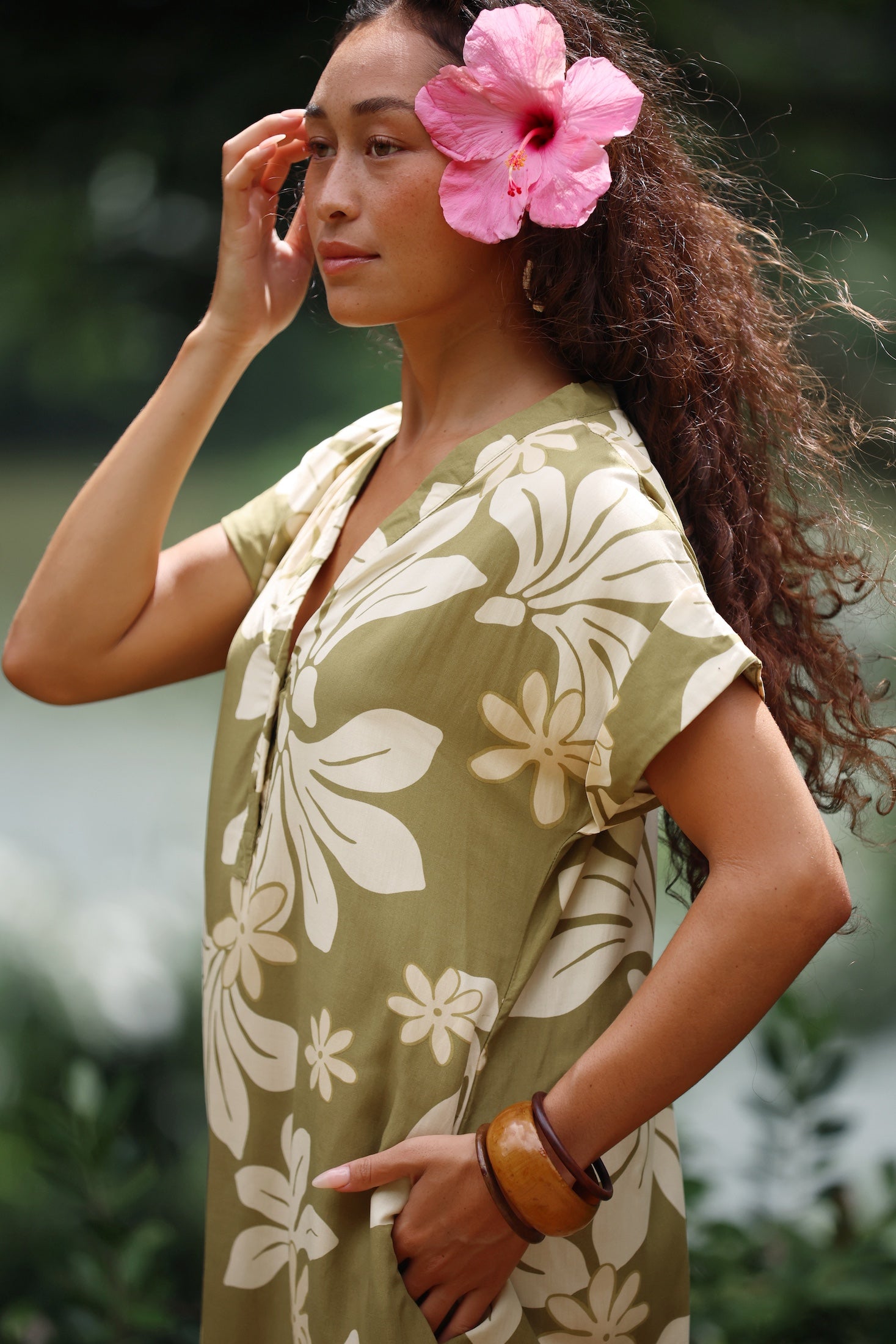 woman with brown hair wearing a maxi dress in a green color with naupaka pattern throughout.