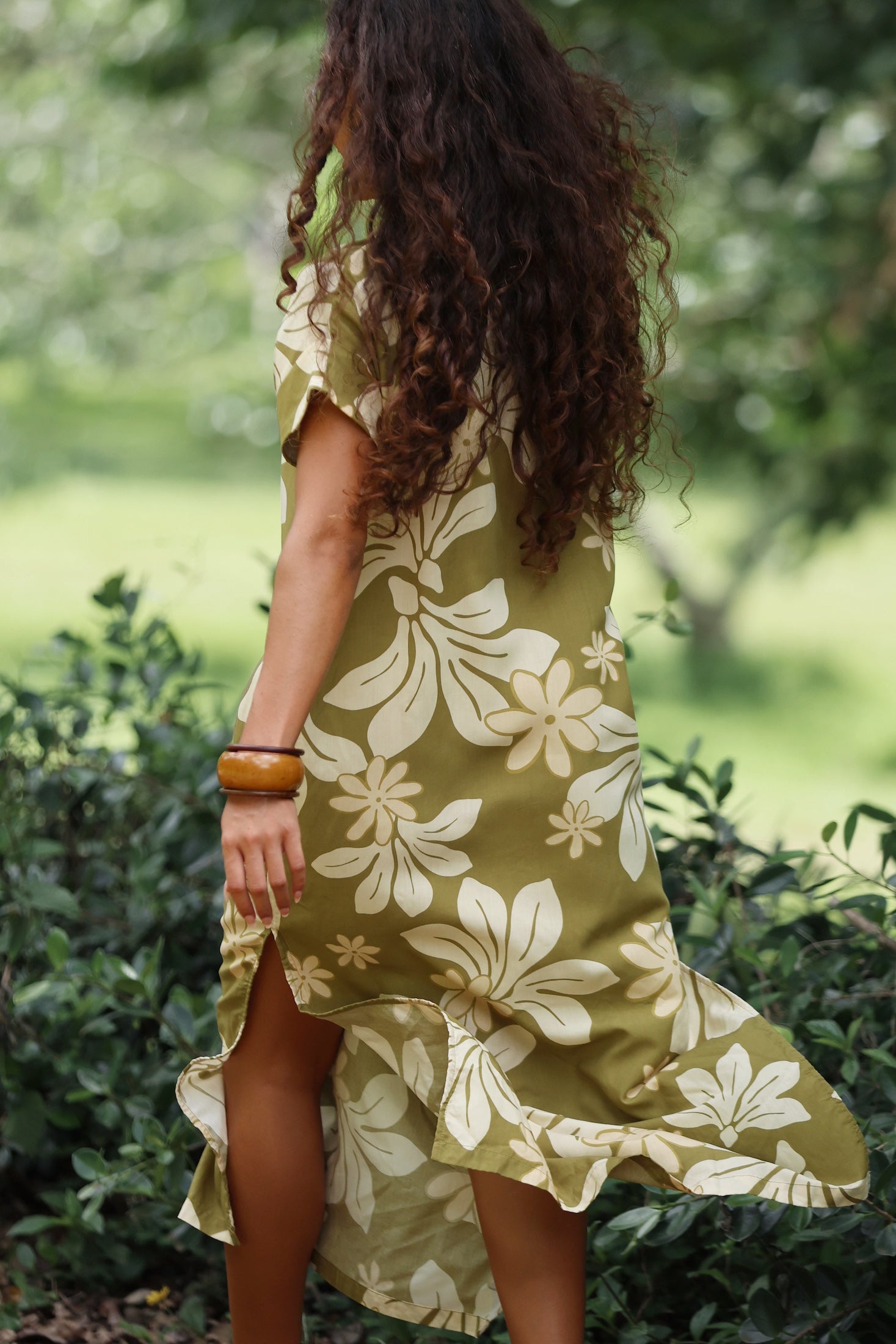 woman with brown hair wearing a maxi dress in a green color with naupaka pattern throughout.