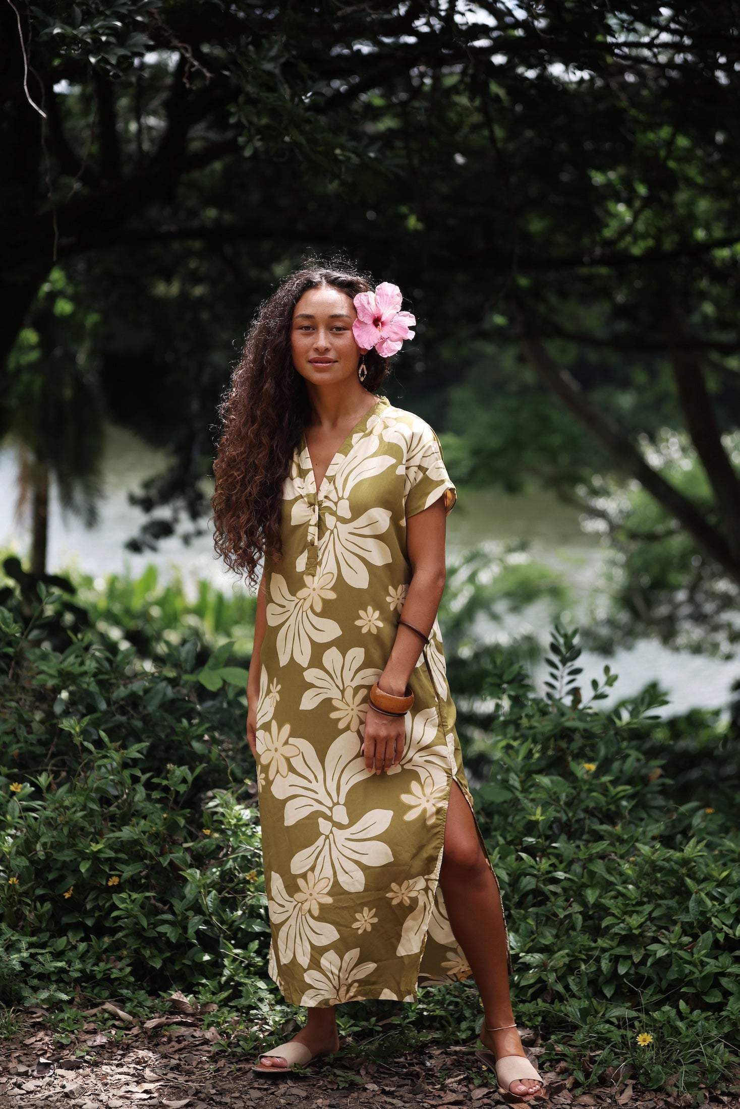 woman with brown hair wearing a maxi dress in a green color with naupaka pattern throughout.