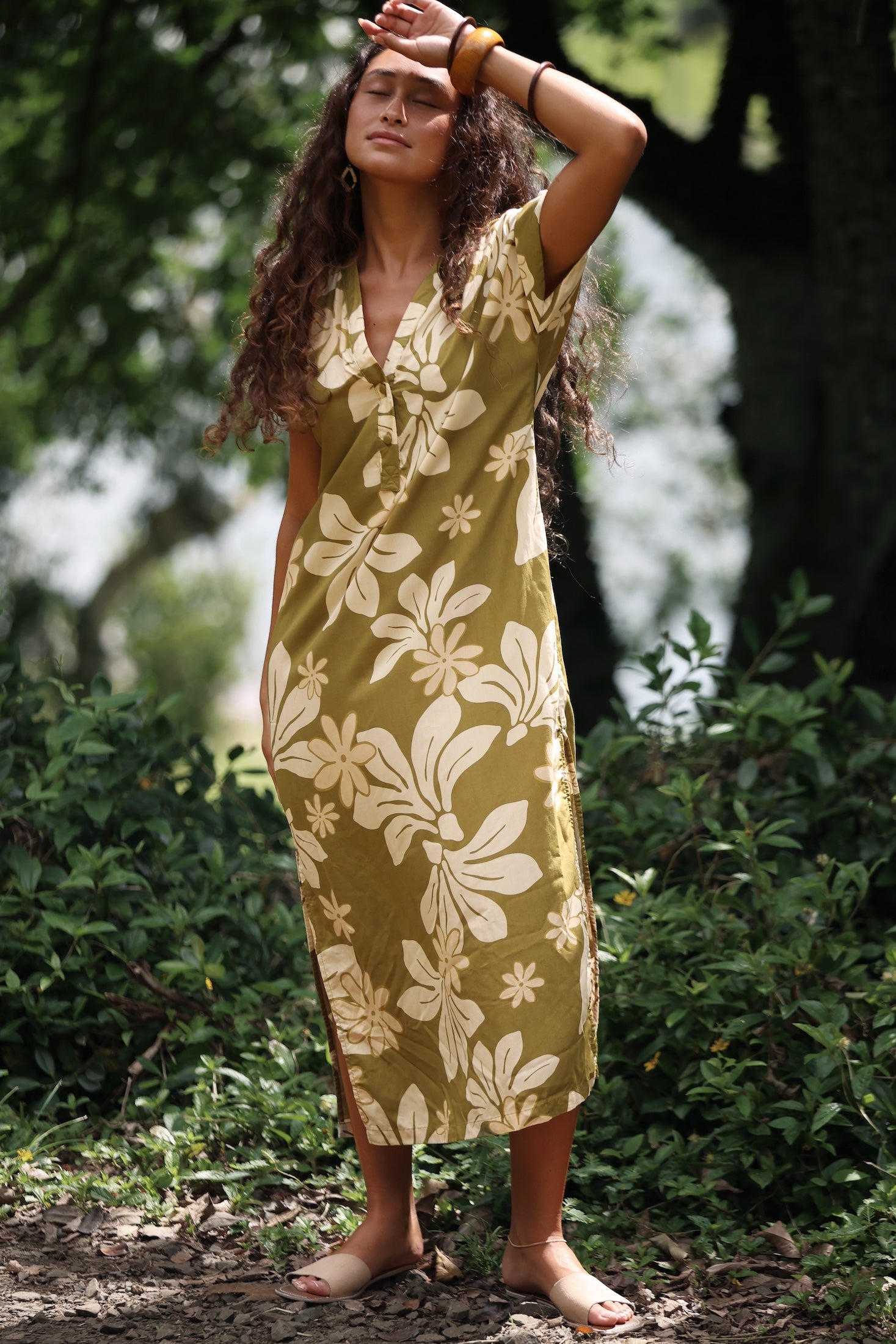 woman with brown hair wearing a maxi dress in a green color with naupaka pattern throughout.
