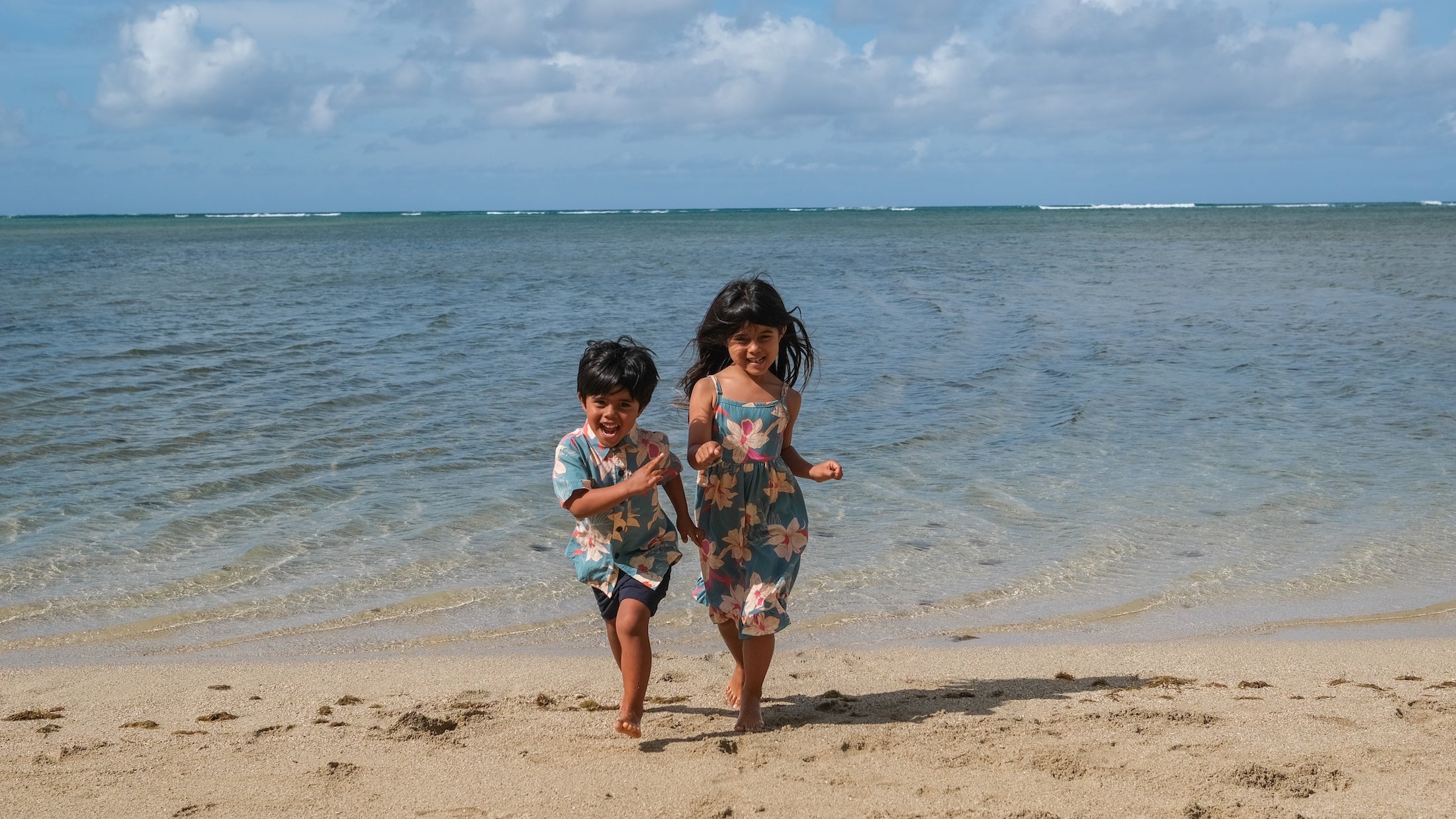 little boy wearing a teal aloha shirt with cream colored orchid blossom pattern