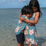 little boy wearing a teal aloha shirt with cream colored orchid blossom pattern