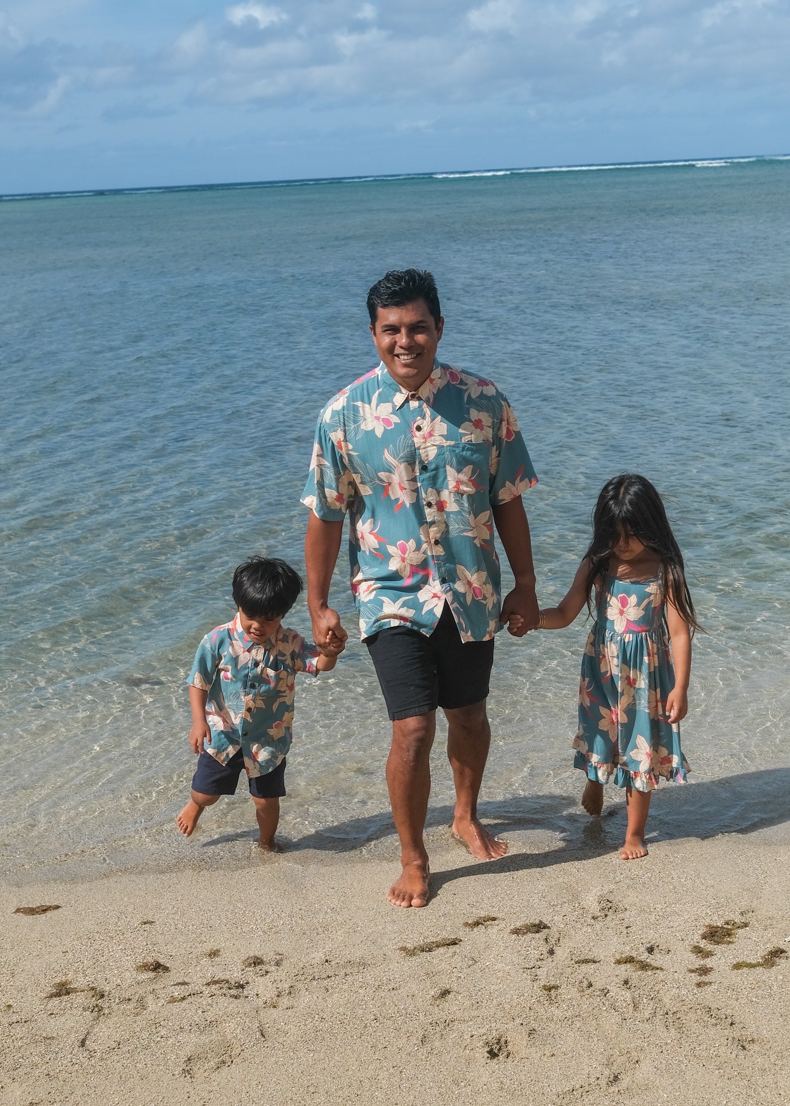 little boy wearing a teal aloha shirt with cream colored orchid blossom pattern
